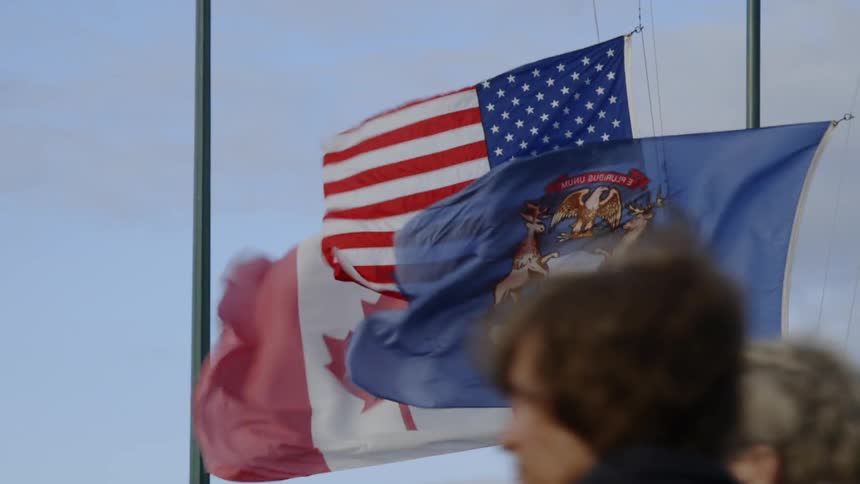People walk past flags blowing in the wind