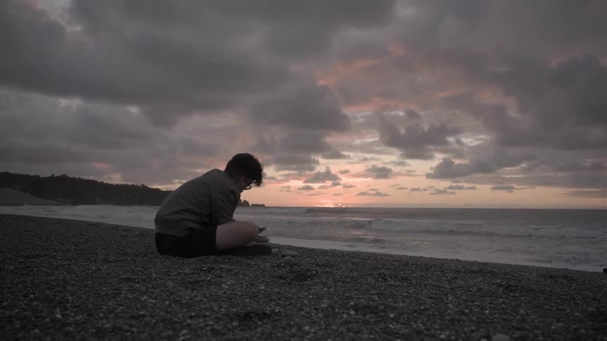 A person sits on a beach at sunset