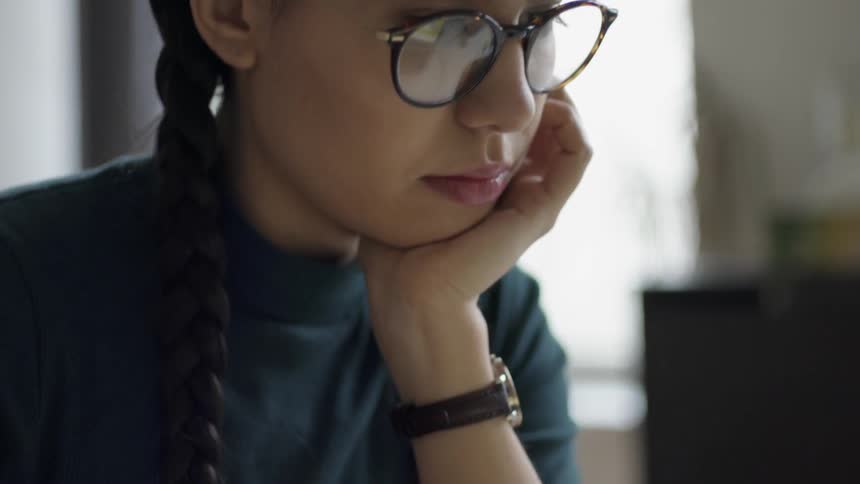 A woman in glasses scrolls on a laptop
