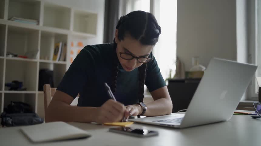 A woman writes on a sticky note at a desk