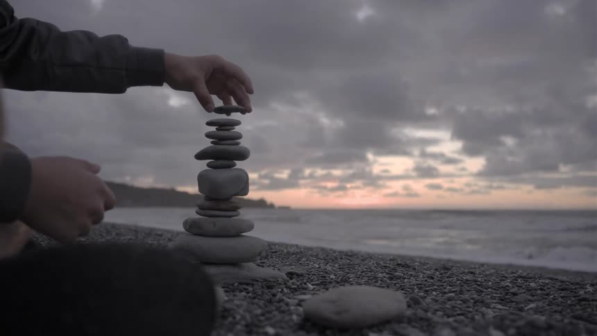 The person is stacking rocks on the beach