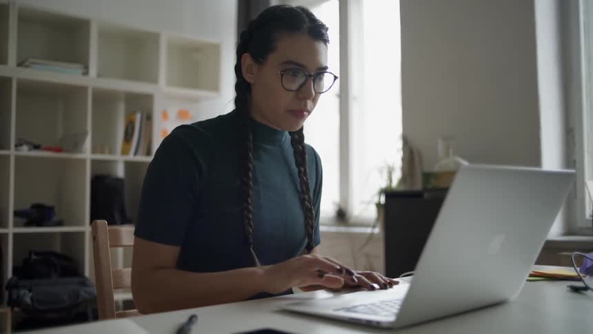 Woman wearing glasses sits down and begins to work on a laptop