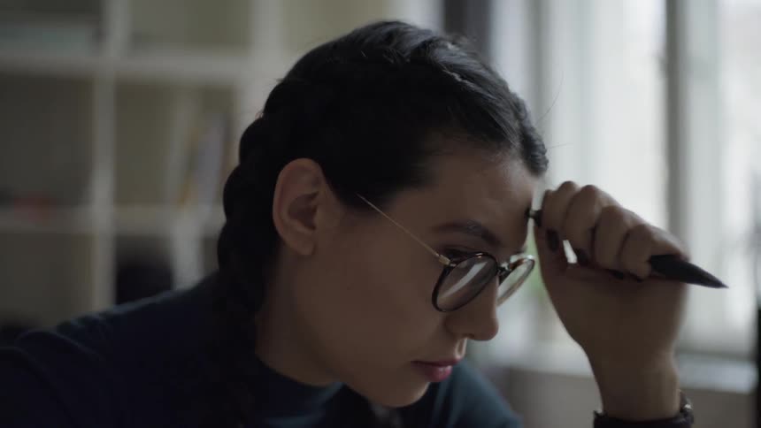 The woman taps a pen against her head