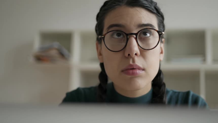 A woman wears glasses while working on a laptop