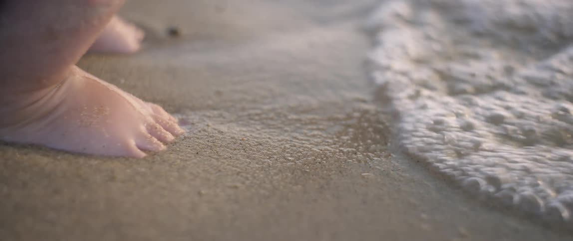 Water flows over the feet of a young girl on the beach