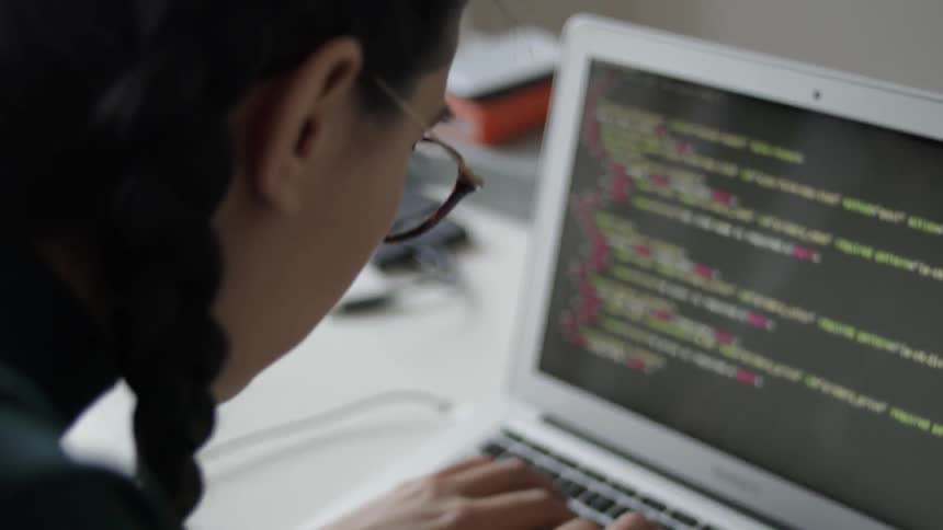 A woman in glasses types on a laptop