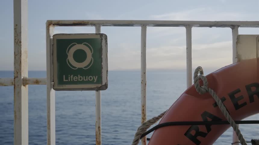 Orange life preserve and a rope sits near the railing as the boat travels in the water