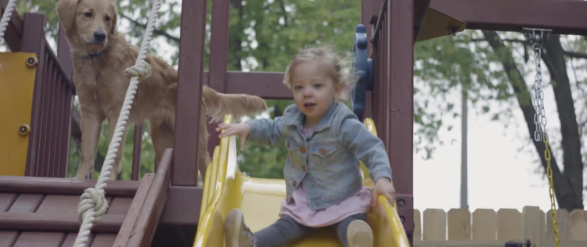 A toddler girl goes down a slide in a backyard