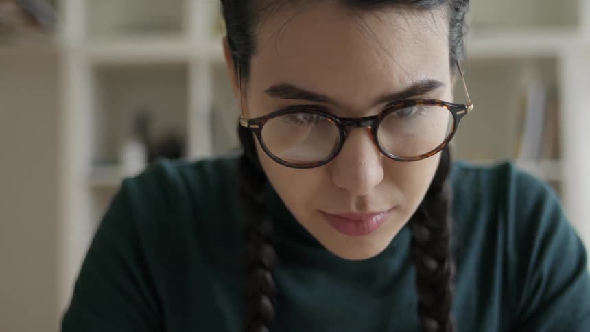 A woman wearing glasses is reading while she sits working inside in daylight