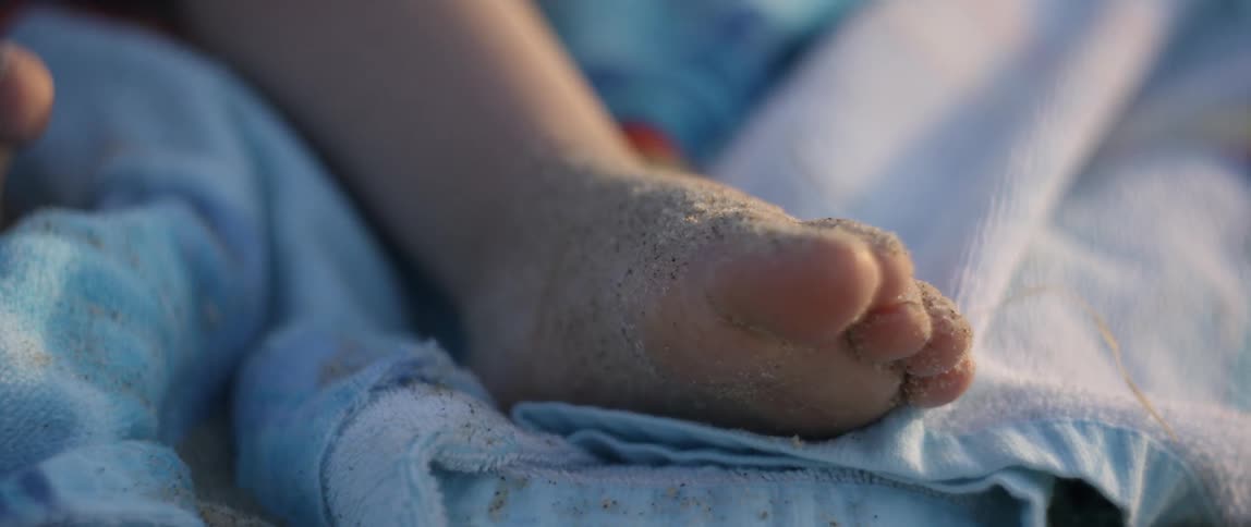 A young girls sandy leg sits atop the towels