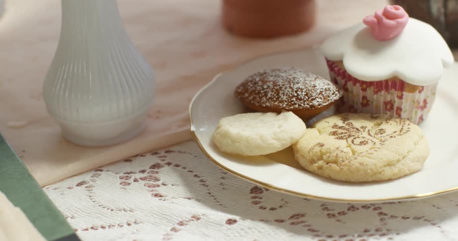 A plate with cookies and a cupcake sitting on a white table cloth