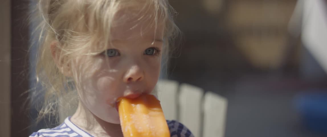 Little girl with blond hair eats a frozen treat