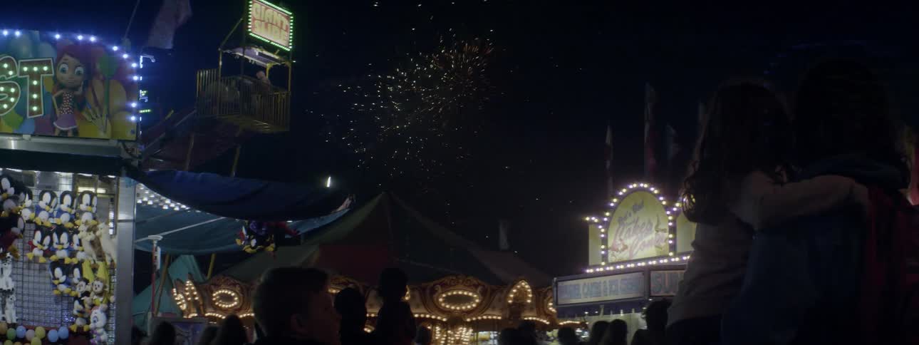 The people walk around the carnival as the fireworks go off