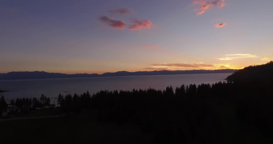 A view of trees, water and mountains as the sun sets