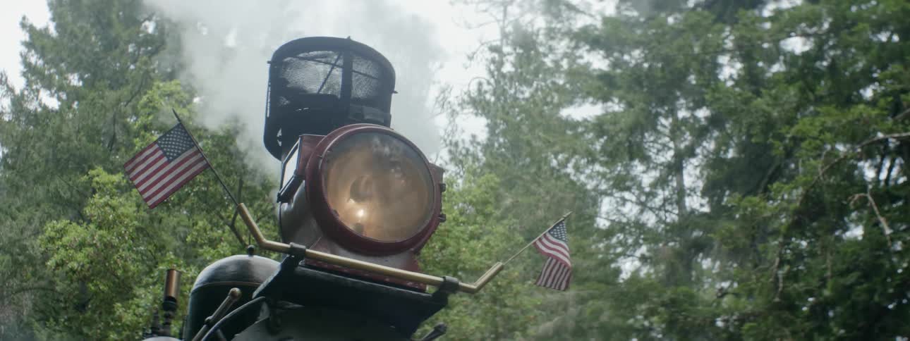 Steam shoots out of a steam engine as it sits near the trees