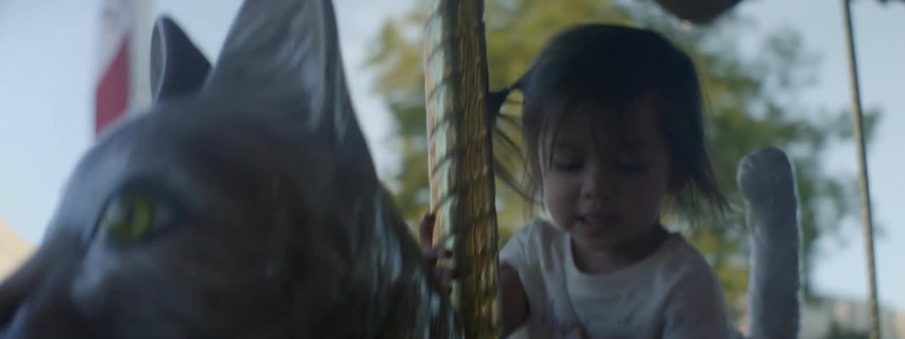 A toddler girl is riding on a carousel at a fair in daylight