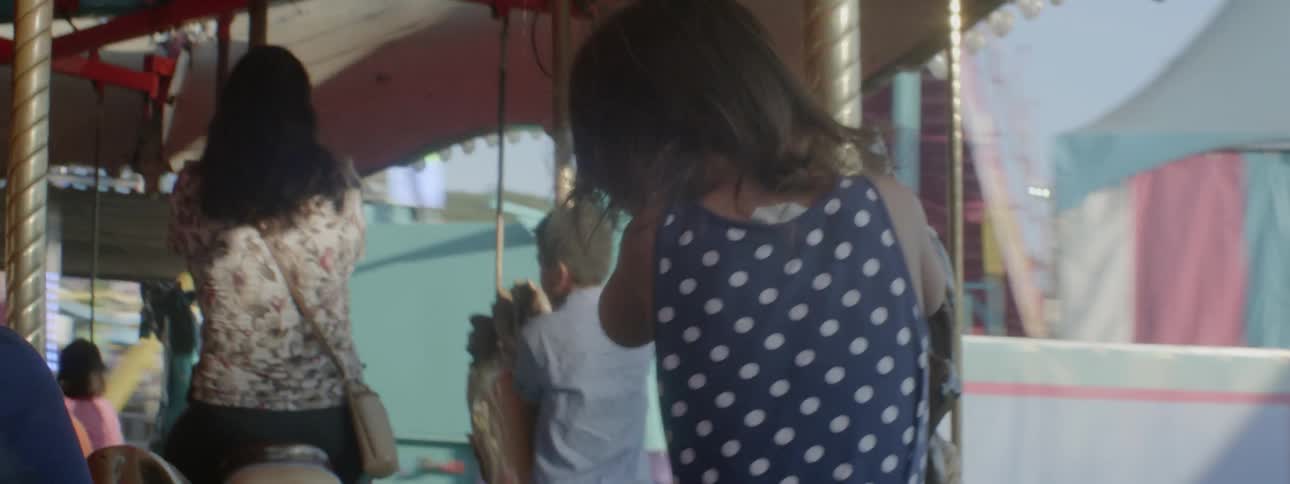 A little girl is riding on a carousel at a fair on a sunny day