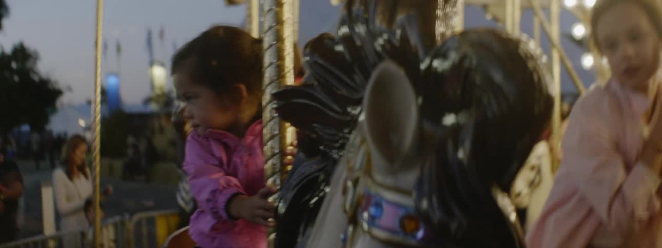 Little girl sits on a carousel horse as it goes up and down