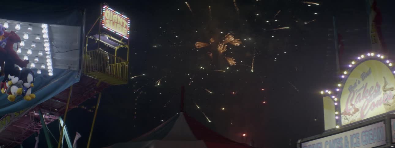 Fireworks are exploding in the sky above fairground rides at night