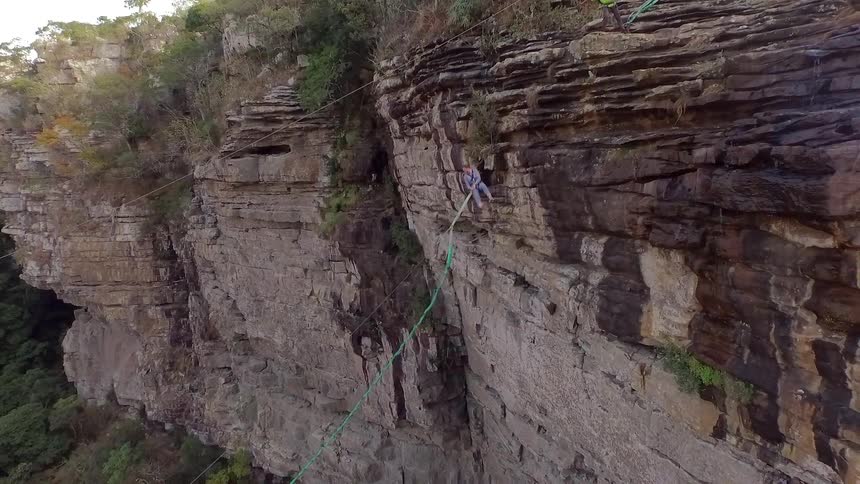 A man pushing a woman, who is holding a rope, off the side of a cliff