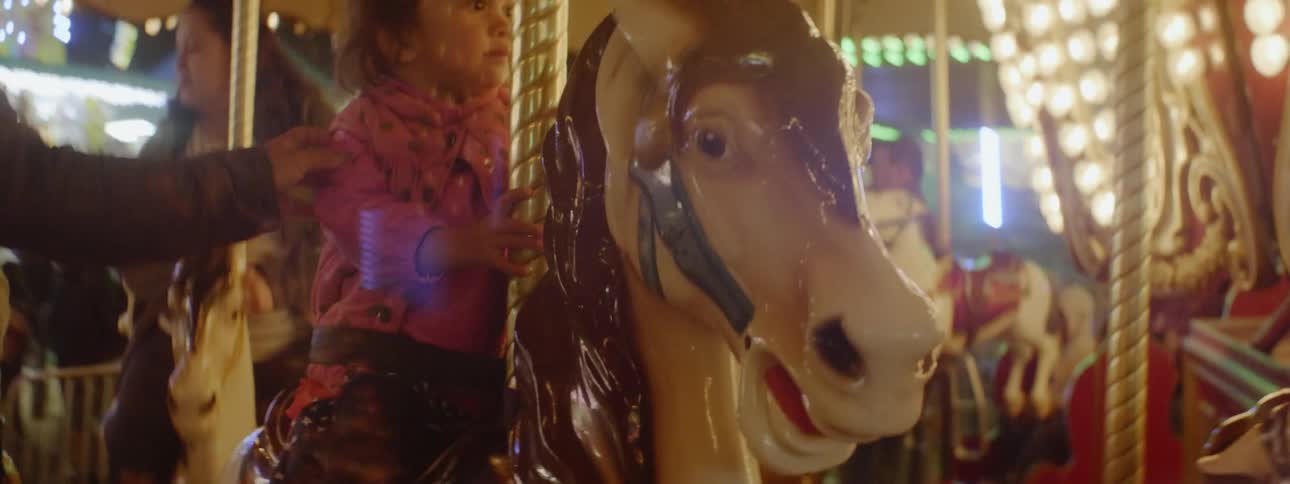 A little girl is riding on a carousel at a fair at dusk