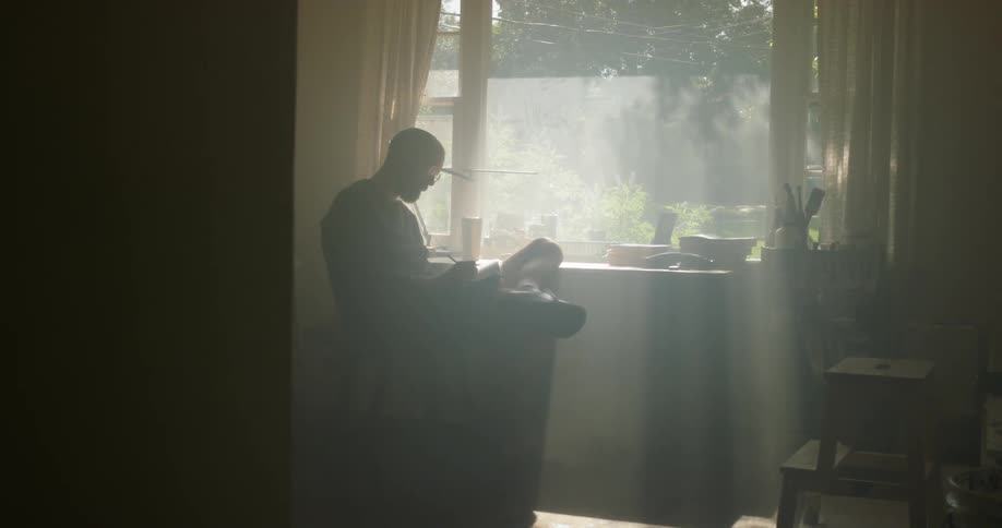 A man writes at a desk next to a sunny window