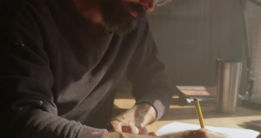 A man is sitting at a desk at home drawing in a notebook in daylight
