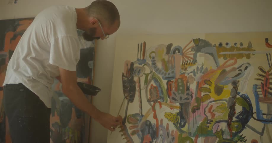 An artist is painting on a large canvas inside in daylight