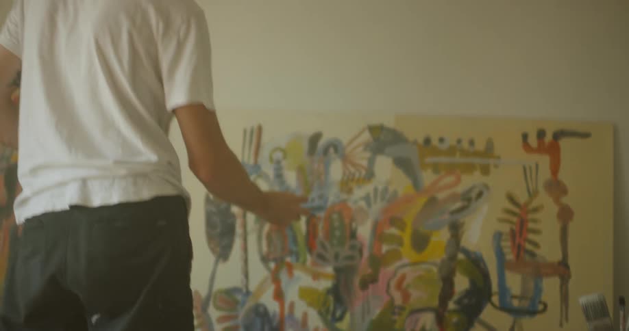 A man is mixing paint on a palette then painting on a canvas inside in daylight