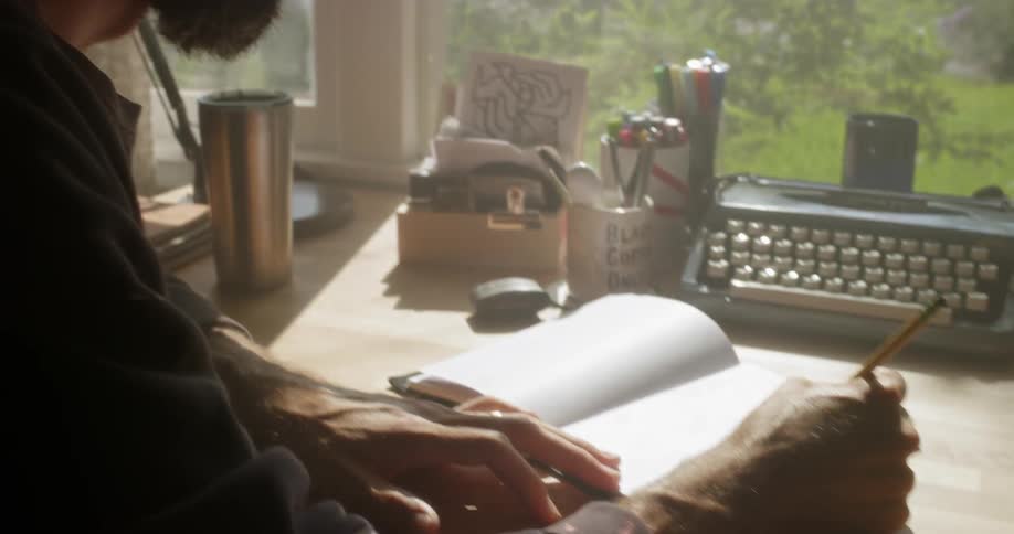 The man is wearing glasses writing at his desk