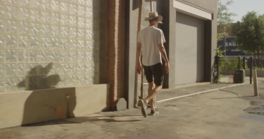 A man adjusts his cowboy hat while walking on a sidewalk