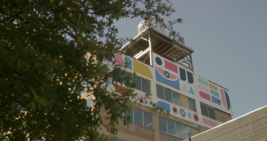 An airplane is flying over a building painted with colorful geometric shapes during the day