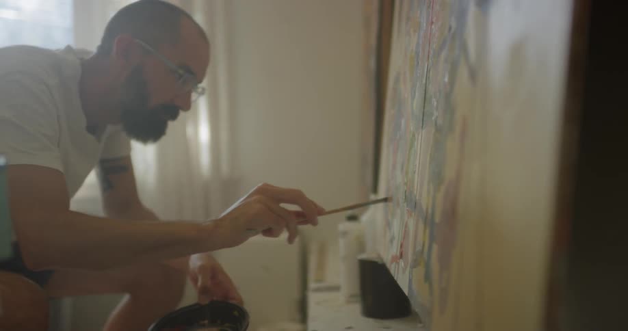 An artist is painting on a large canvas inside in daylight