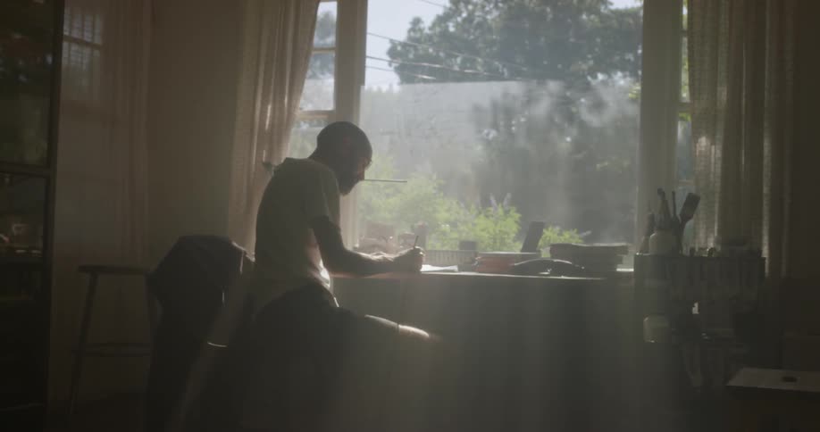The man is writing at his desk by the window