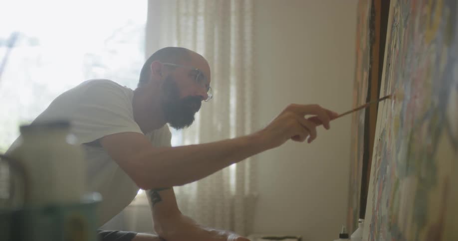 An artist is painting on a large canvas inside in daylight
