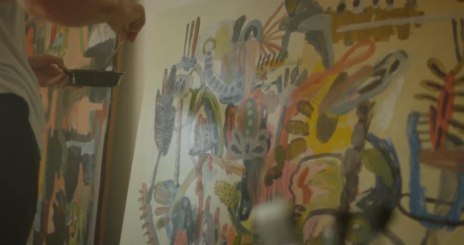 An artist is painting on a large canvas inside in daylight