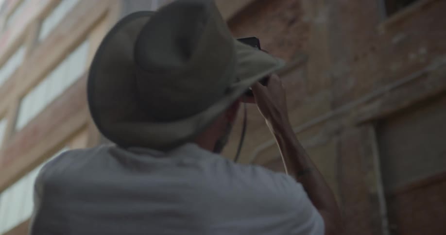 A man is taking a photograph of a building with a cell phone then walking away in daylight