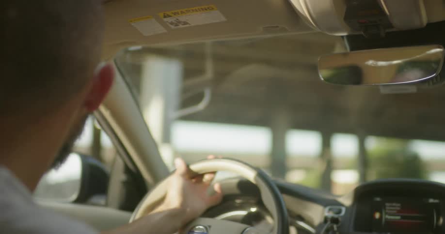 A man is driving a car beneath a freeway overpass on a sunny day