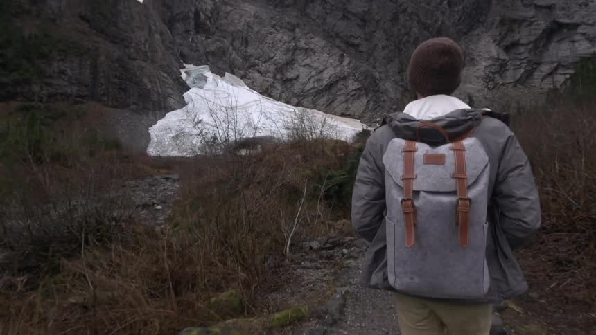 A hiker wearing a backpack walks towards a mountain