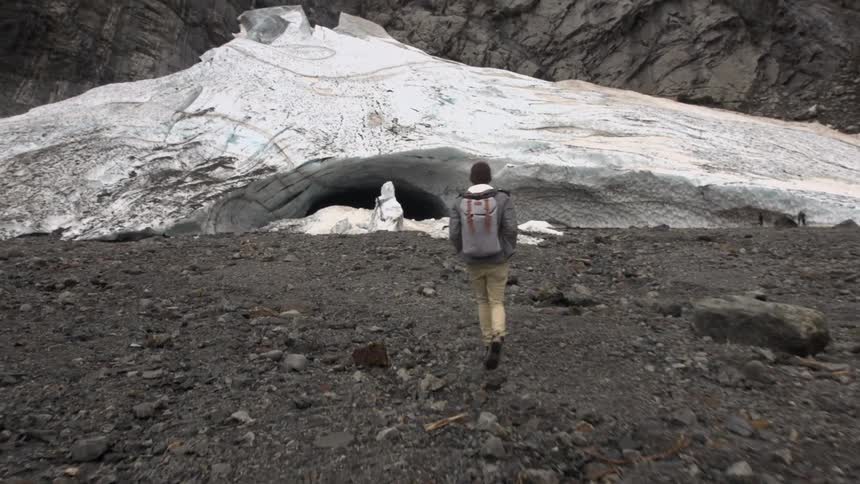 Man walks over rocky terrain towards a cave