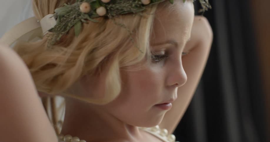 A young girl wearing a wreath on her head and a fancy wedding-style dress