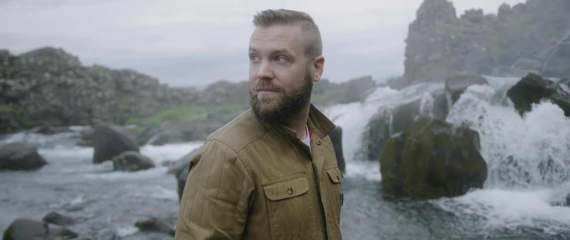 A man stands near waterfalls on an overcast day