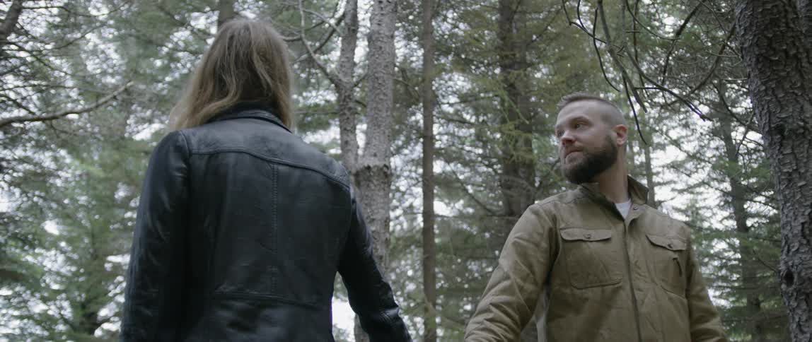 A man and woman hold hands in a forest