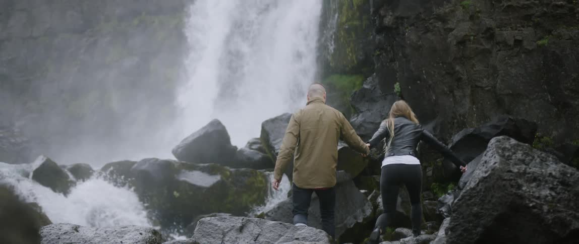 A couple climb over the rocks by the waterfall