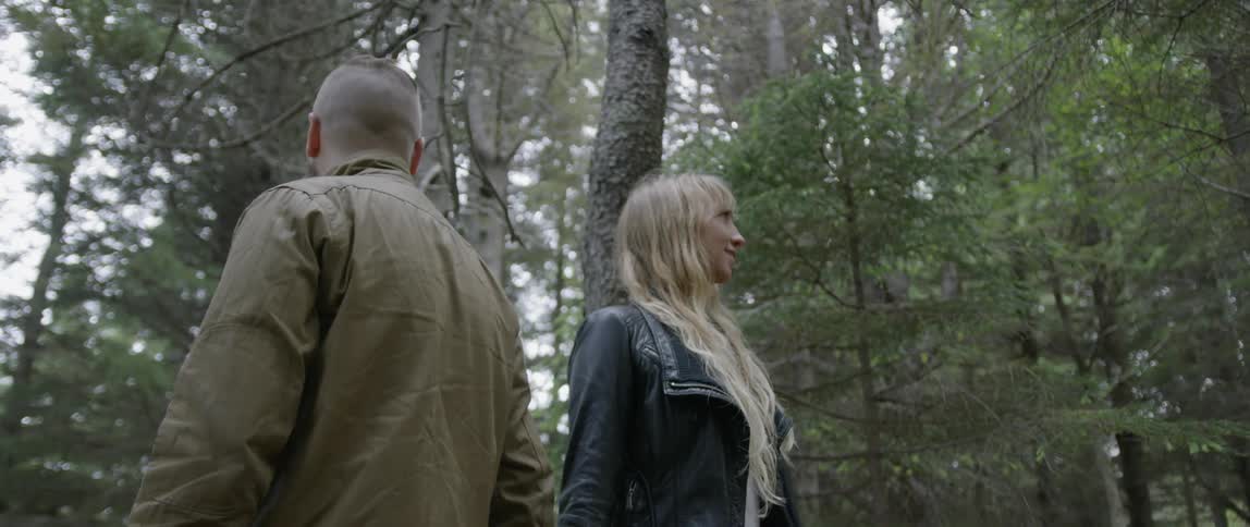 A man and woman hold hands while standing in a forest