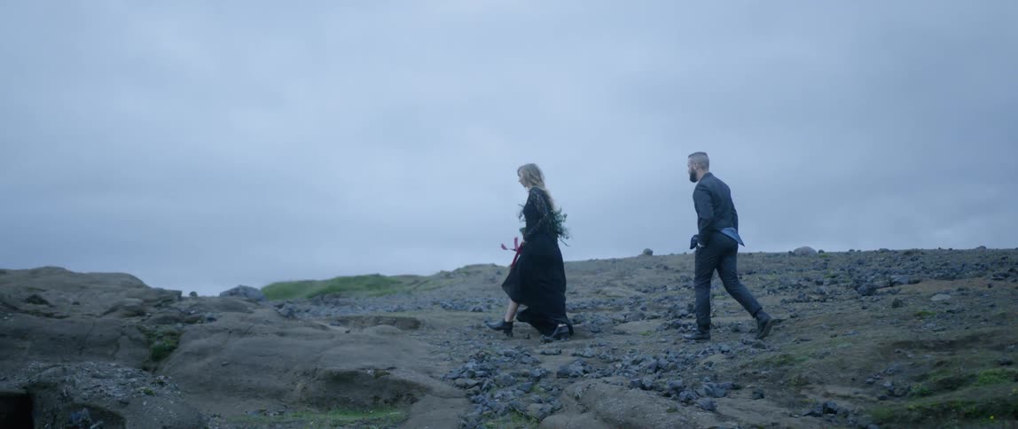 A man and woman walk over dirt and rocks on an overcast evening
