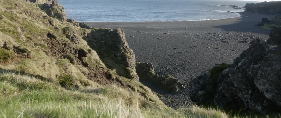 Waves roll into the sandy beach near the grassy hills