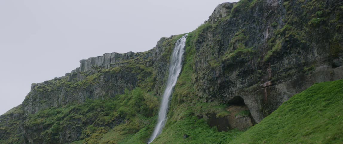 The tall waterfall has green on both sides