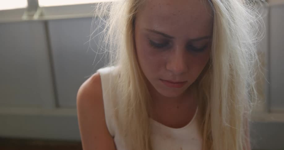 A blonde woman is sitting on the floor looking down
