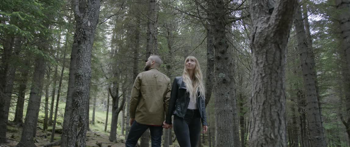 A man and woman hold hands in a forest